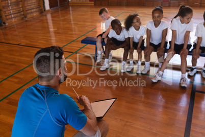 Basketball coach talking with schoolkids at basketball court