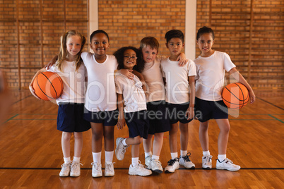 Front view of schoolkids standing and looking at camera at basketball court