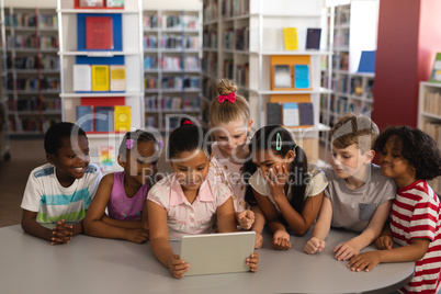 Front view of schoolkids studying together on digital tablet at table