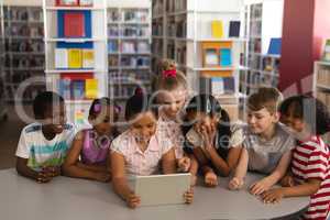 Front view of schoolkids studying together on digital tablet at table