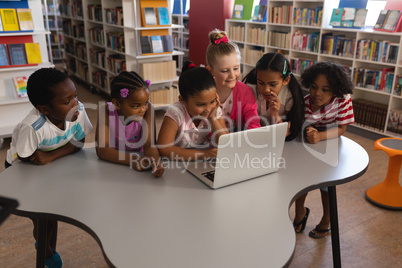 Schoolkids studying together on laptop at table in school library