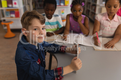 Smiling schoolboy holding digital tablet and looking at camera in school library