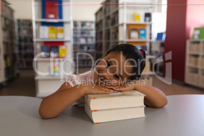 Happy schoolgirl leaning on books and looking at camera on table in school library