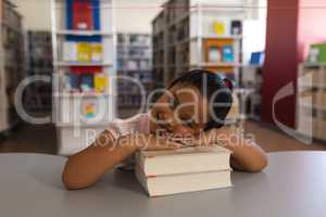 Happy schoolgirl leaning on books and looking at camera on table in school library