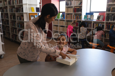 Female school teacher teaching her student at table in school library