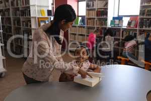 Female school teacher teaching her student at table in school library