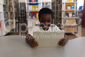 Happy schoolboy studying on digital tablet at table in school library