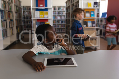 Thoughtful schoolboy with hand on chin looking away sitting at table in school library