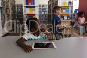 Thoughtful schoolboy with hand on chin looking away sitting at table in school library