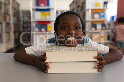 Happy schoolboy leaning his face on books and looking at camera on table