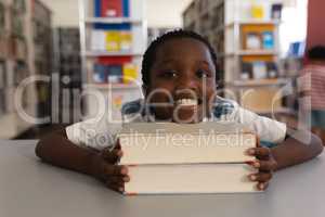 Happy schoolboy leaning his face on books and looking at camera on table