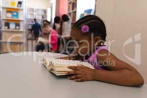 Schoolgirl reading book at table in in school library