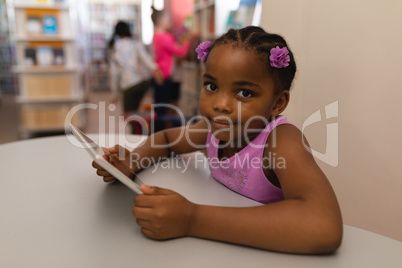 Schoolgirl with digital tablet looking at camera on table in school library