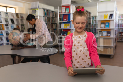 Schoolgirl studying on digital tablet at table in school library