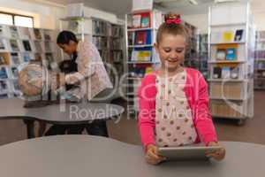 Schoolgirl studying on digital tablet at table in school library