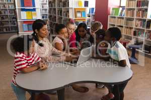 Female teacher teaching schoolkids on laptop at table in school library