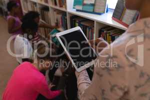Female teacher working on digital tablet in school library