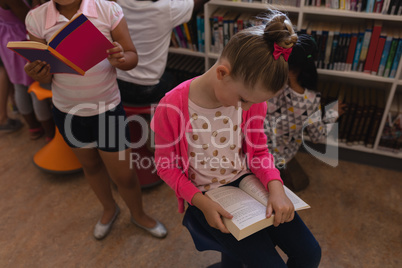Schoolgirl reading a book and sitting on chair in school library