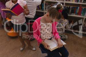 Schoolgirl reading a book and sitting on chair in school library