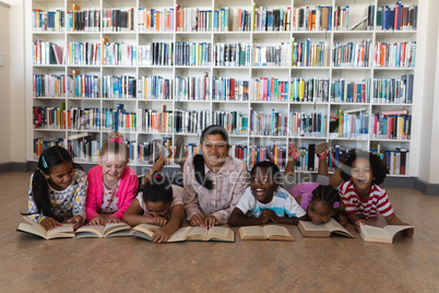 Female teacher and schoolkids reading a book while lying on floor of school library