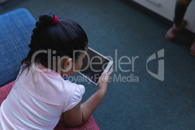 Schoolgirl studying on digital tablet while lying on the couch in school library