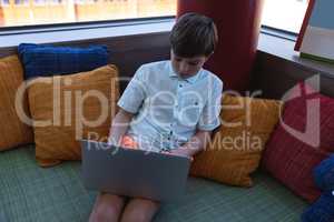 Schoolboy studying on laptop while siting on the couch in school library