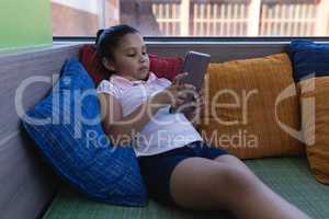 Schoolgirl studying on digital tablet while siting on the couch in school library