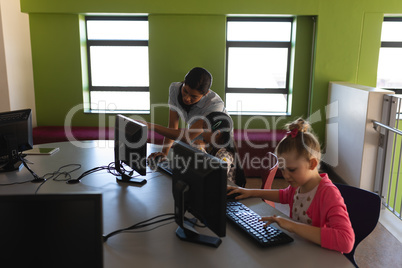 Female teacher teaching computer to schoolkid at desk in school