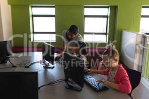 Female teacher teaching computer to schoolkid at desk in school