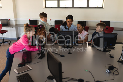 Female teacher teaching computer to schoolkids at desk in school