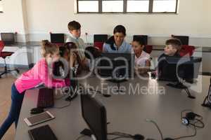 Female teacher teaching computer to schoolkids at desk in school