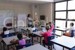 Female teacher explaining skeleton parts to schoolkids in classroom
