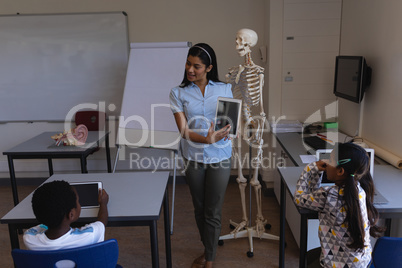Female teacher teaching schoolboy on digital tablet at table in classroom
