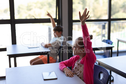 School kids raising their hand while sitting at desk in classroom