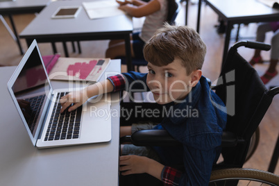 Disable schoolboy studying on laptop while sitting at desk in classroom
