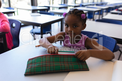 Schoolgirl sitting at desk and looking at camera in classroom