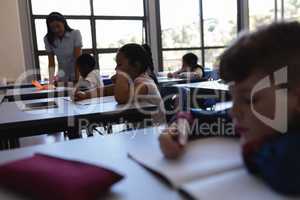 Female teacher teaching schoolkid at desk in classroom