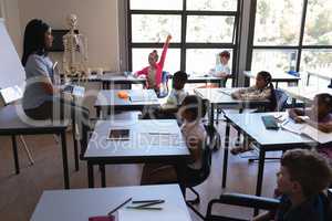 Female school teacher teaching schoolkids on laptop in classroom