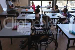 Disable schoolboy with classmates studying and sitting at desk in classroom