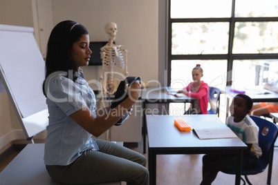 Female teacher holding and looking at virtual reality headset in classroom