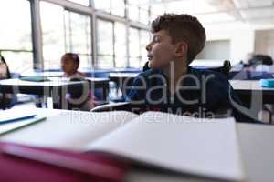 Schoolboy sitting at desk and looking away in classroom