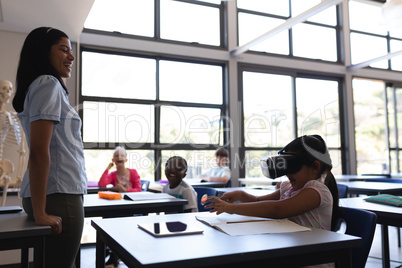 School girl using virtual reality headset at desk in classroom