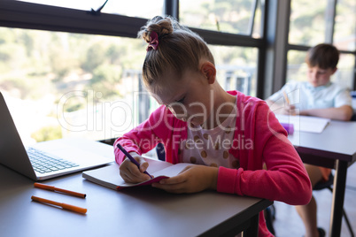 Schoolgirl writing on notebook at desk in classroom