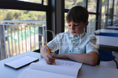 Schoolboy drawing on notebook at desk in classroom