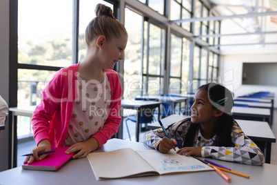 Schoolkids talking with each other at desk in classroom