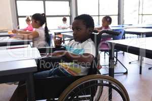Thoughtful disable schoolboy looking away at desk in classroom