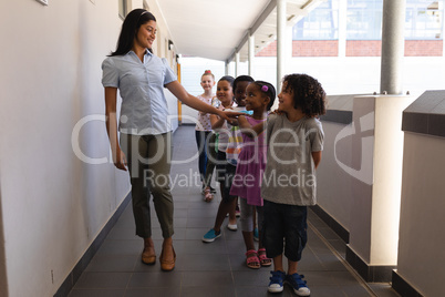 Schoolkids with teacher standing in row with their hands on shoulder in hallway