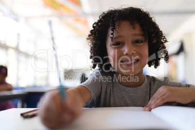 Happy schoolboy looking at camera at desk in classroom