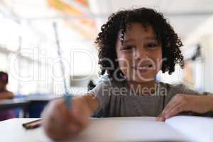 Happy schoolboy looking at camera at desk in classroom