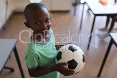 Smiling schoolboy holding football in classroom